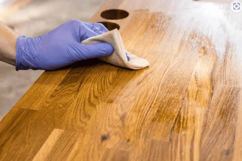 Produits de finition Une main gantée de mauve utilise un chiffon pour appliquer un produit de finition sur un meuble en bois, mettant en évidence le processus de finition d'un projet d'intérieur.